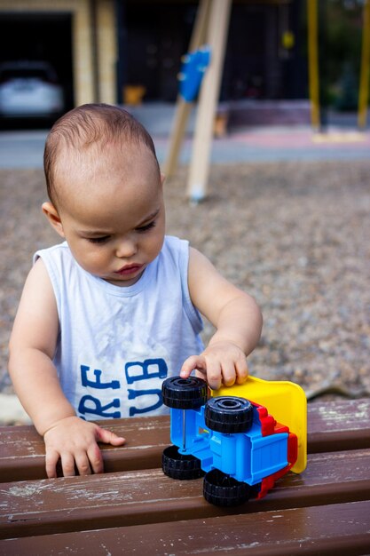 Nettes glückliches lächelndes Baby, das draußen mit buntem Spielzeugauto auf dem Kinderspielplatz spielt