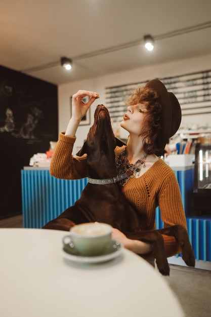 Foto nettes hipster-mädchen verbringt zeit in einem tierfreundlichen café mit einem welpen in ihren armen