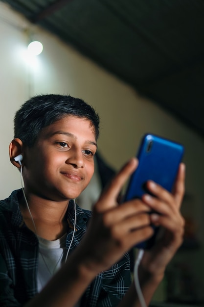 Nettes indisches Kind, das Smartphone und Kopfhörer Gadget verwendet