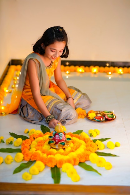 Nettes indisches kleines Mädchen, das zu Hause Dekoration mit Blumen- und Öllampe für das Diwali-Fest macht