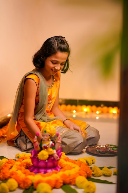 Nettes indisches kleines Mädchen, das zu Hause Dekoration mit Blumen- und Öllampe für das Diwali-Fest macht