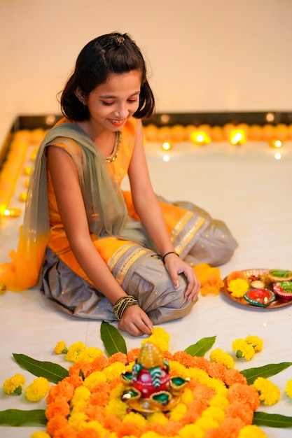 Nettes indisches kleines Mädchen, das zu Hause Dekoration mit Blumen- und Öllampe für das Diwali-Fest macht