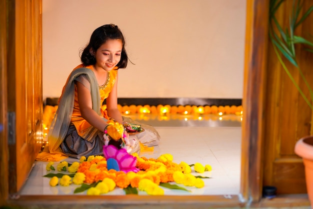 Nettes indisches kleines Mädchen, das zu Hause Dekoration mit Blumen- und Öllampe für das Diwali-Fest macht