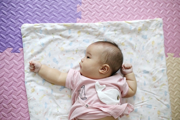 Nettes intelligentes asiatisches neugeborenes Baby, das zu Hause mit Teddybärkaninchenspielzeug auf rosa weichem Bett schläft.