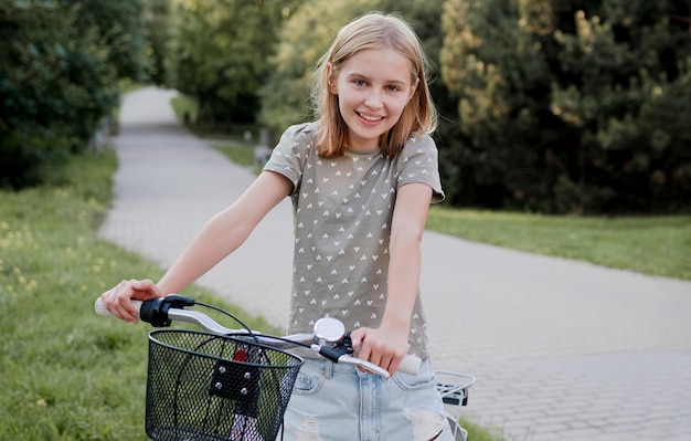 Nettes jugendliches Mädchen mit Fahrrad im Freien, das in die Kamera blickt und hübsches Kind mit Fahrrad in der Stadt lächelt