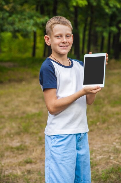 Nettes junges kaukasisches Kind, das mit Tablette im Park arbeitet