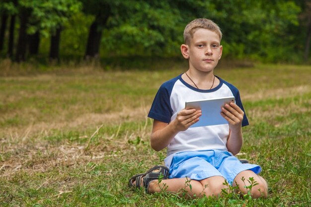 Nettes junges kaukasisches Kind, das mit Tablette im Park arbeitet