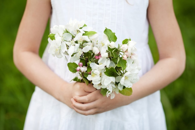 Nettes junges Mädchen, das einen Blumenstrauß von Apfelblumen hält. Schönes Mädchen im weißen Kleid im Garten mit blühenden Apfelbäumen.