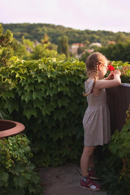 Nettes junges Mädchen in einem schönen Kleid, das mit Blumen auf dem Balkon spielt