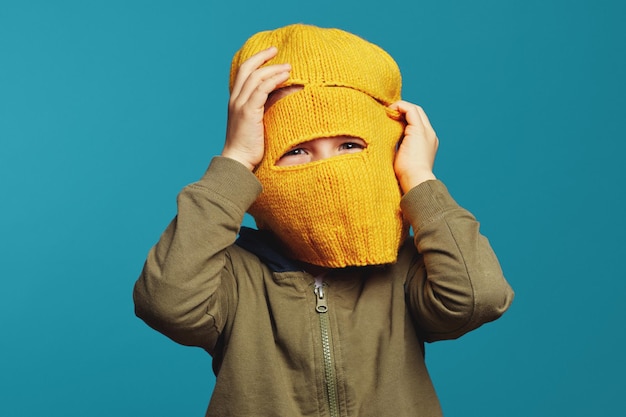 Foto nettes kind, das die kamera durch die gelbe gestrickte diebmaske betrachtet, die über isoliert ist