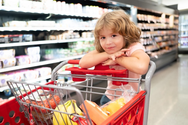 Nettes Kind mit Einkaufswagen im Lebensmittelgeschäft oder Supermarkt