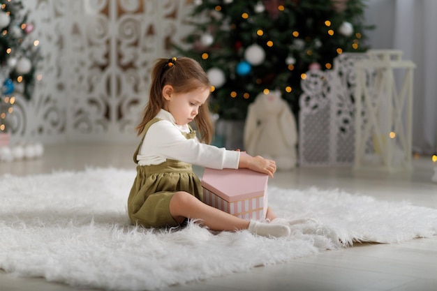 Nettes Kindermädchen, das Neujahrsgeschenk hält, während es auf dem weißen Teppich sitzt