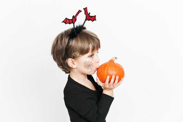 Nettes Kindermädchen in schwarzem Kostüm und Make-up mit Kürbis, der Spaß an der Halloween-Feier hat