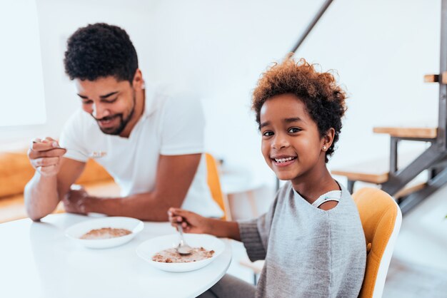 Nettes kleines Afroamerikanermädchen, das gesundes Frühstück mit ihrem Vati isst.