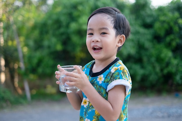 Nettes kleines asiatisches Jungenlächeln und Griffwasserglas für gesundes Trinken