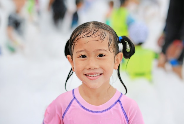 Nettes kleines asiatisches Kindermädchen der Nahaufnahme, das Spaß in der Schaum-Partei am Pool im Freien habend lächelt.