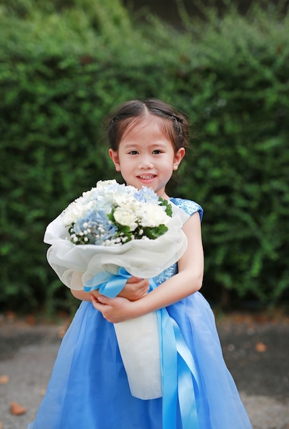 Nettes kleines asiatisches Kindermädchen mit Blumenstrauß von Blumen im Garten