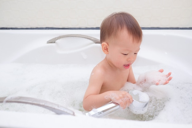 Nettes kleines asiatisches Kleinkindbabykind, das Spaß hat, in der Badewanne zu sitzen