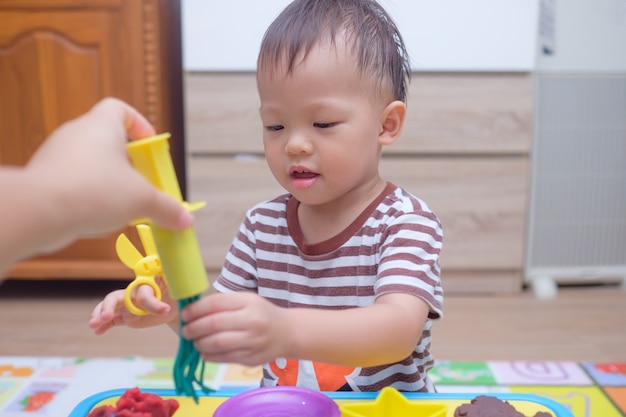 Nettes kleines asiatisches kleinkindjungenkind, das spaß hat, bunte modelliermasse spielt teig zu hause spielt