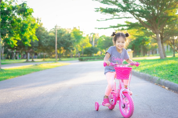 Nettes kleines asiatisches Mädchen, das Fahrrad fährt, um im Park, im Kindersport und im aktiven Lebensstil zu üben