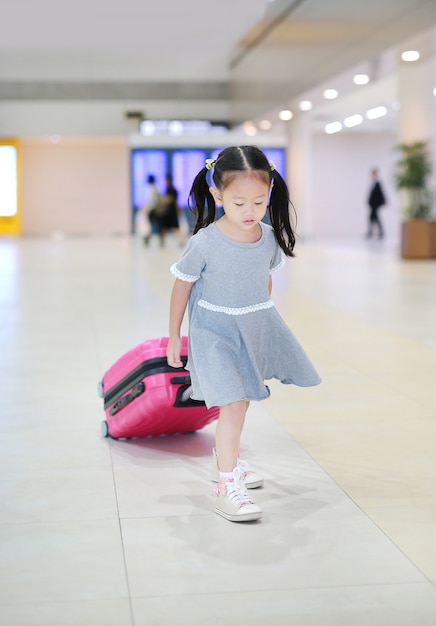 Nettes kleines asiatisches Mädchen, das mit Gepäck am Flughafen geht