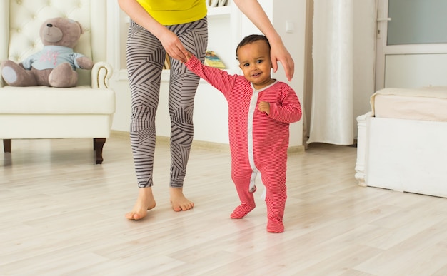 Nettes kleines Baby, das laufen lernt, Mama hält seine Hände.