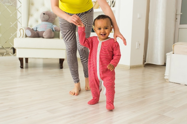 Nettes kleines Baby, das laufen lernt, Mama hält seine Hände.