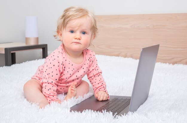 Nettes kleines Baby mit Laptop im Elternschlafzimmer