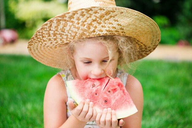 Nettes kleines blondes Mädchen, das Wassermelone isst, Sommer im Freien.