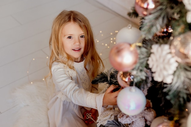 Nettes kleines blondes Mädchen im Kleid nahe Weihnachtsbaum