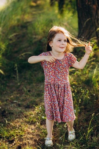 Nettes kleines blondes Mädchen in einem weißen Kleid, das den Weg im Wald hinuntergeht, die Aussicht von hinten