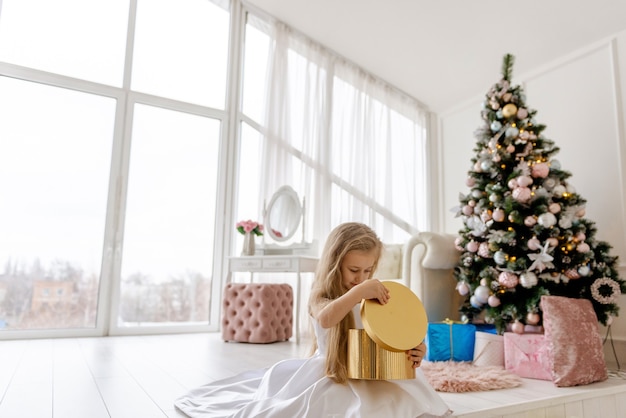 Nettes kleines blondes Mädchen öffnet ein Weihnachtsgeschenk. Fröhliches Weihnachtsbaby.