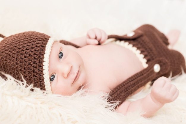 Nettes kleines glückliches Baby liegt in einem Bärenkostüm auf einem Weiß. Neugeborenes in einem Hut mit Ohren auf einem weißen