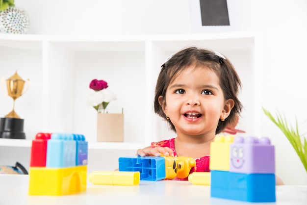 Nettes kleines indisches asiatisches Mädchen, das beim Spielen mit Spielzeug oder Blöcken genießt und am Tisch sitzt