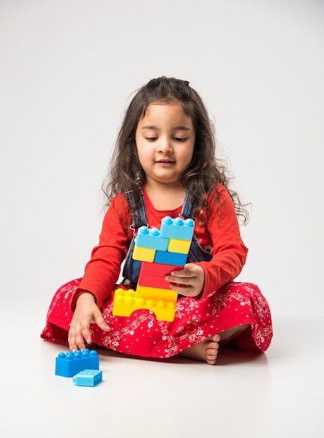 Nettes kleines indisches asiatisches Mädchen, das mit bunten Blockspielzeugen auf weißem Hintergrund spielt