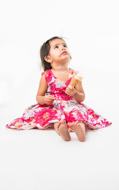 Nettes kleines indisches asiatisches Mädchenkind, das Schokoladeneis im Kegel leckt oder isst, lokalisiert auf weißem Hintergrund