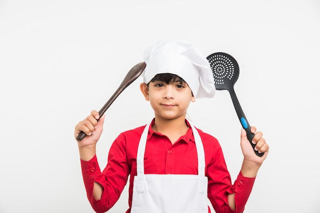 Nettes kleines indisches Kind oder Junge, das als Koch verkleidet ist und Kochutensilien hält, isoliert auf weißem Hintergrund
