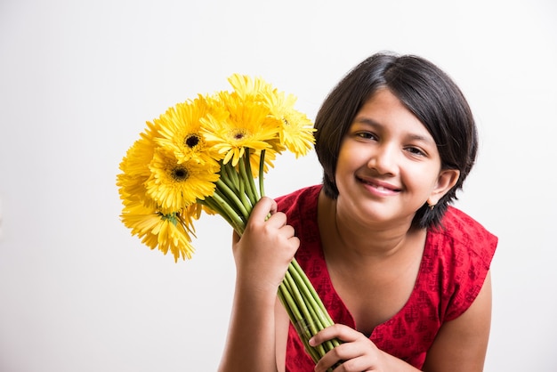 Nettes kleines indisches Mädchen, das einen Haufen oder einen Blumenstrauß frischer gelber Gerberablumen hält. Auf weißem Hintergrund isoliert