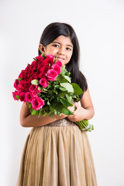 Nettes kleines indisches Mädchen, das einen Haufen oder einen Strauß frischer roter Rosen oder Gulab-Blumen hält. Auf weißem Hintergrund isoliert