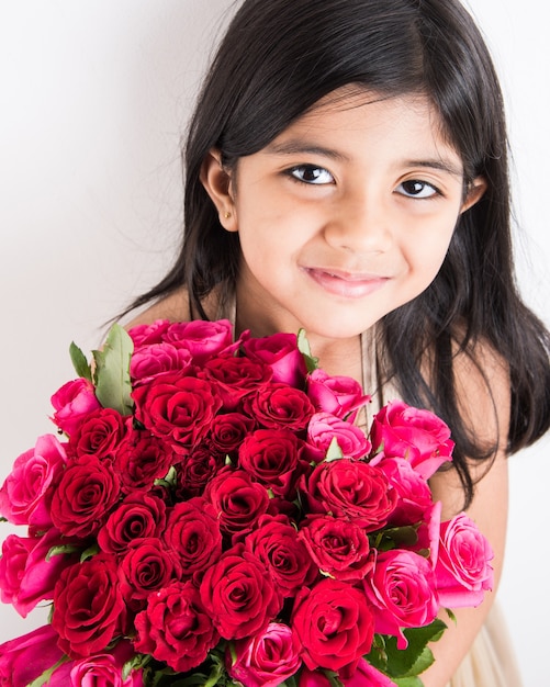 Nettes kleines indisches Mädchen, das einen Haufen oder einen Strauß frischer roter Rosen oder Gulab-Blumen hält. Auf weißem Hintergrund isoliert