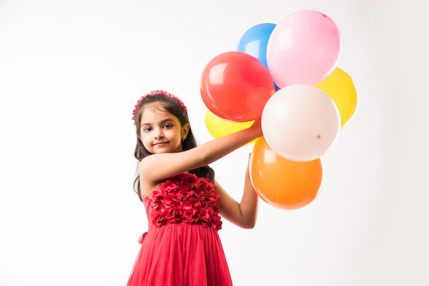 Nettes kleines indisches oder asiatisches Mädchen mit bunten Luftballons oder gubbare in Hindi, über weißem oder rotem Hintergrund