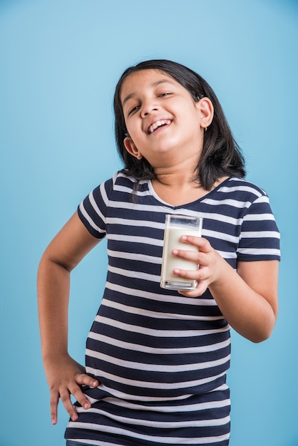 Nettes kleines indisches oder asiatisches verspieltes Mädchen, das ein Glas Milch hält oder trinkt, einzeln auf buntem Hintergrund