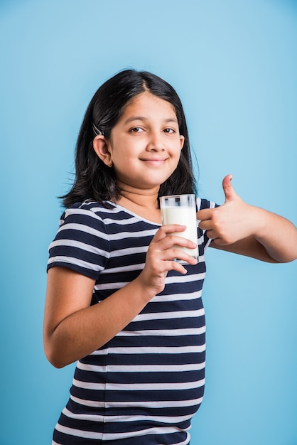 Nettes kleines indisches oder asiatisches verspieltes Mädchen, das ein Glas Milch hält oder trinkt, einzeln auf buntem Hintergrund