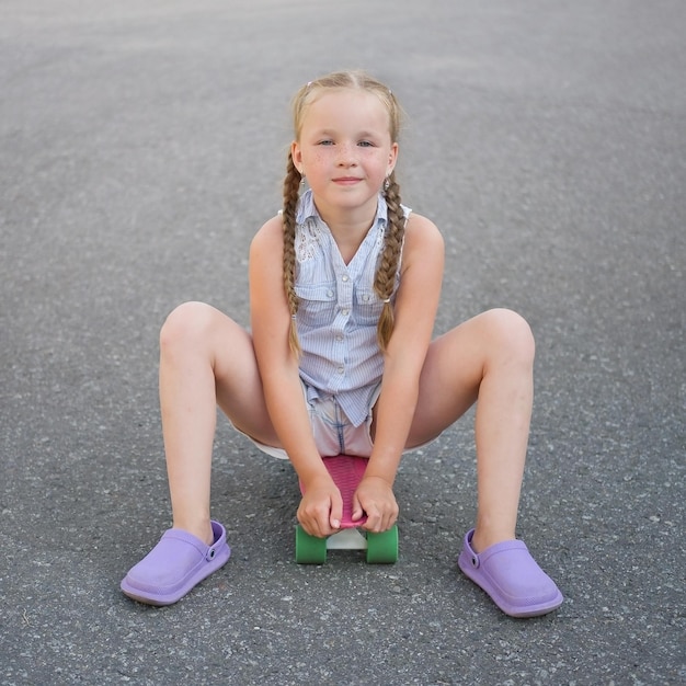 Nettes kleines jugendliches Mädchen sitzt auf Skateboard