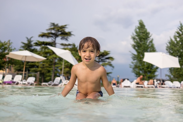 Nettes kleines Jungenkind, das im Schwimmbad spritzt, das Spaßfreizeitaktivität hat