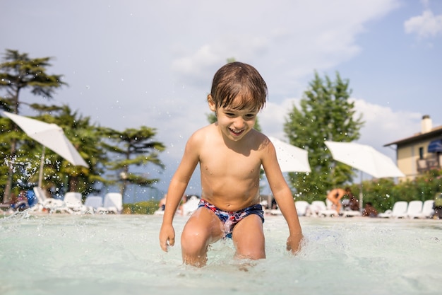 Nettes kleines Jungenkind, das im Schwimmbad spritzt, das Spaßfreizeitaktivität hat