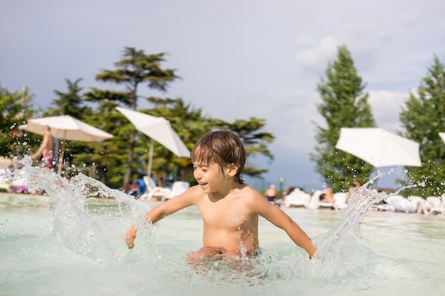 Nettes kleines Jungenkind, das im Schwimmbad spritzt, das Spaßfreizeitaktivität hat