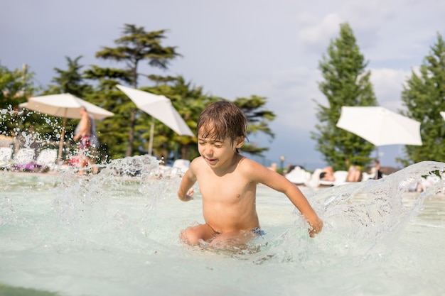 Nettes kleines Jungenkind, das im Schwimmbad spritzt, das Spaßfreizeitaktivität hat