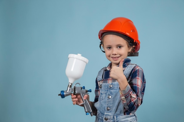 Nettes kleines kaukasisches Kind mit Schutzhelm, das elektrische Spritzpistole hält