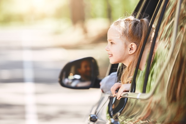 Nettes kleines kaukasisches mädchen, das im auto sitzt und aus der fensterfamilienstraße schaut